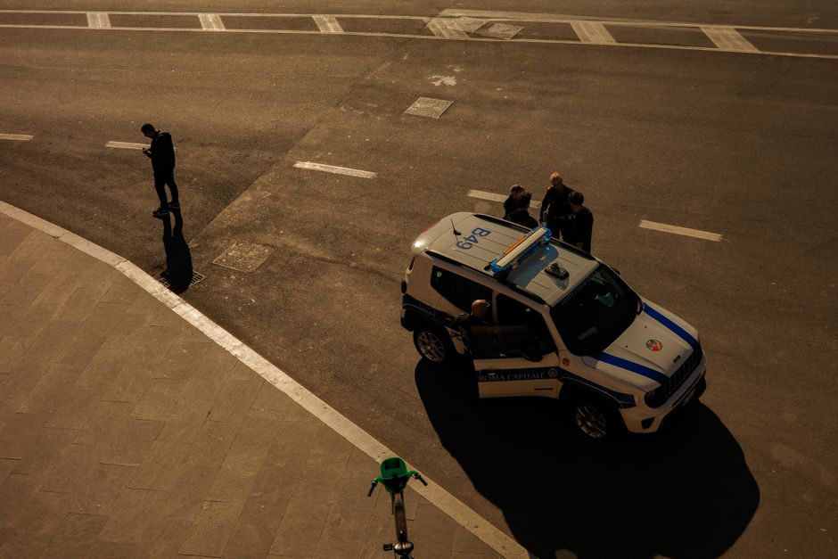 A high-angle view of a police car on the streets of Rome, Italy, with people interacting around it.