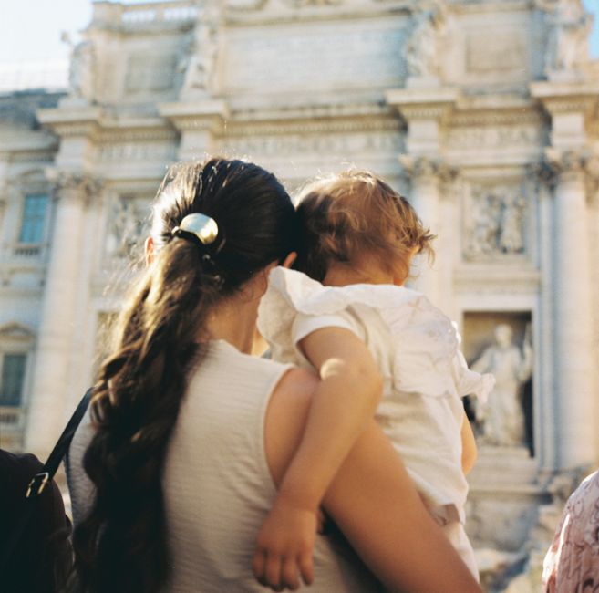 A mother holds her child while standing near the famous Trevi Fountain in Rome, Italy.