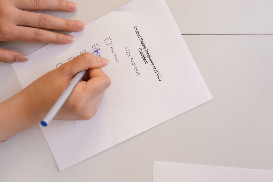 Hand placing vote on ballot form during election process, highlighting civic duty and democracy.