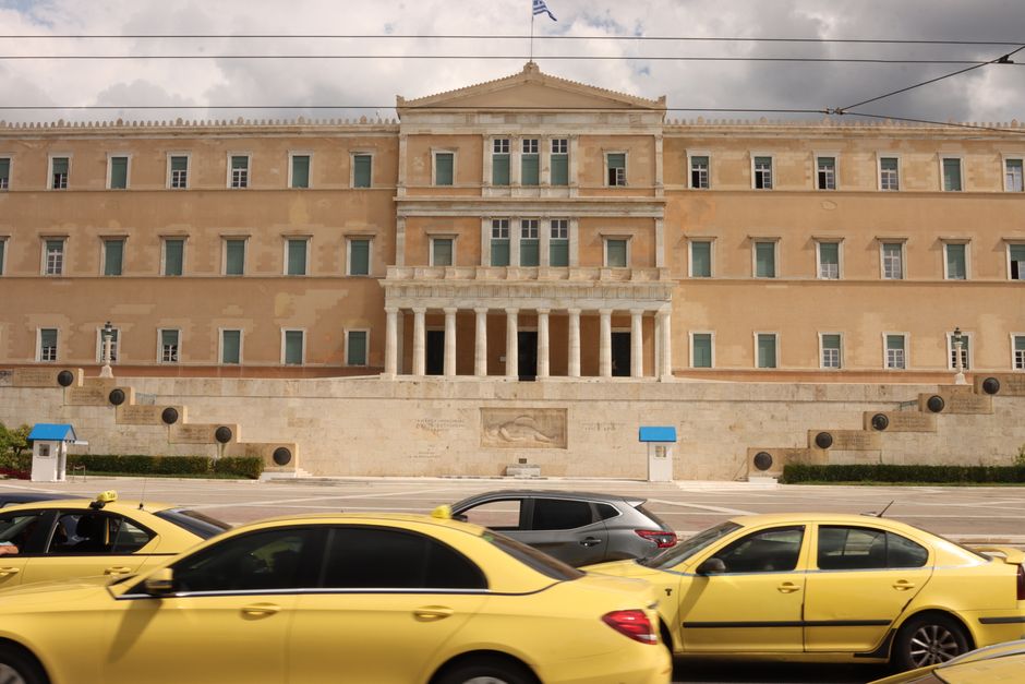 View of the Hellenic Parliament in Athens with yellow taxis in the foreground.